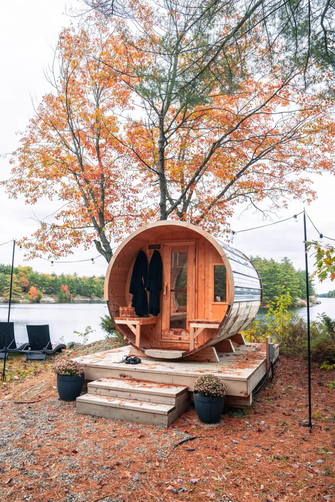 Cedar barrel sauna on a deck beside a lake in autumn